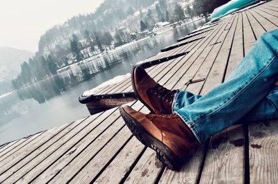 Low section of man relaxing on pier over lake