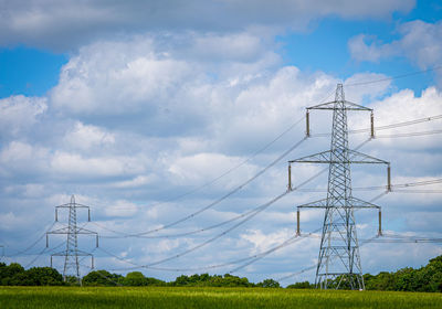 Pylon power electricity electrical distribution cable across field with blue sky and white clouds