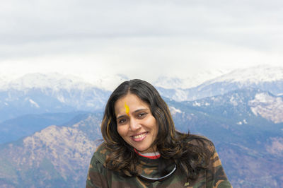 Woman traveler sitting outside kartik swami temple and looking at camera and mountain range.