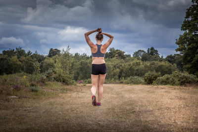 Full length of woman with arms raised on field against sky