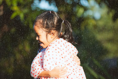 Sisters wearing raincoats embracing in park during rainfall