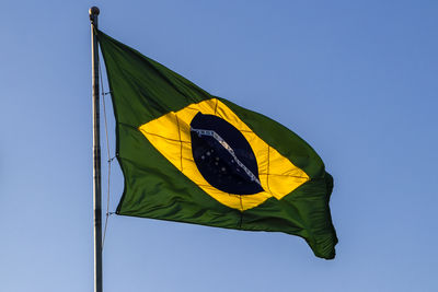 Brazilian flag flutters on a flagpole with the blue sky in the background