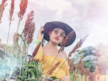 Portrait of young woman wearing hat standing against plants