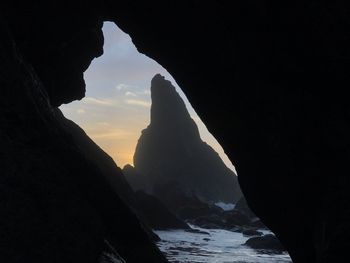 Silhouette rock formation on beach against sky during sunset