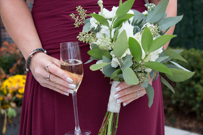 Midsection of woman holding champagne flute and bouquet