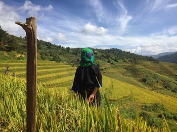 Rear view of woman standing on field against sky