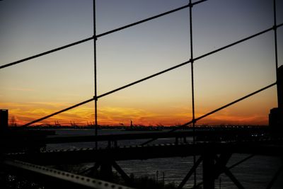 Silhouette bridge over river against sky during sunset