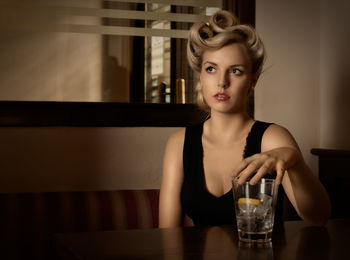 Beautiful young woman with drink sitting at restaurant table