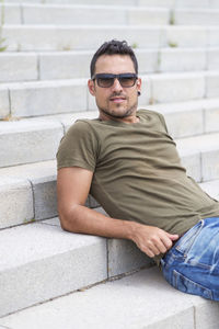 Portrait of young man sitting against wall