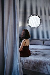 Rear view of woman sitting against curtain