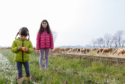 Two children standing in the field next to big flock of sheep