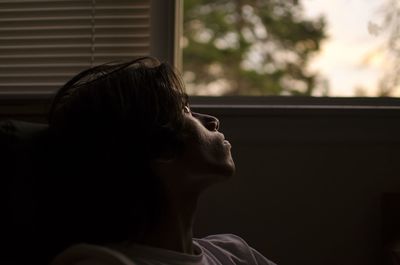 Close-up of teenage boy looking through window at home