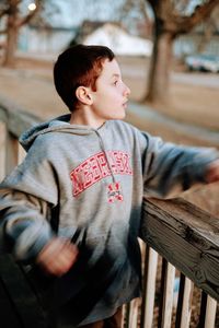 Boy looking away while standing by wooden railing