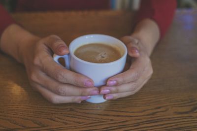 Close-up of hand holding coffee cup on table