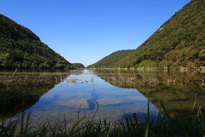 Green mountains by calm lake against clear blue sky