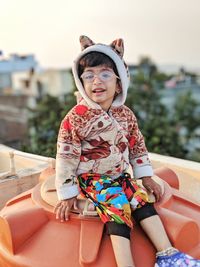 Portrait of smiling girl sitting on building terrace against sky