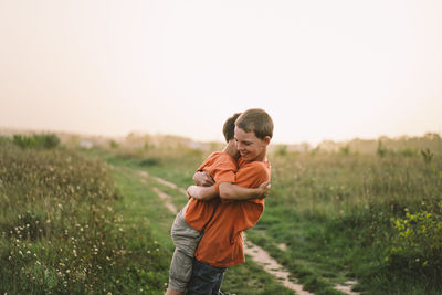 Funny boys brothers in a orange t-shirt playing outdoors on the field at sunset