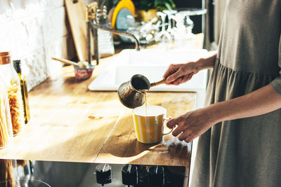 Midsection of woman pouring coffee into cup on table at home