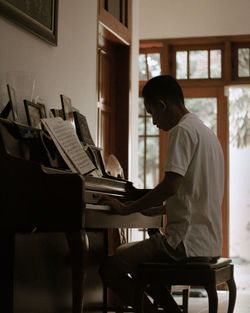 Side view of man playing piano at home