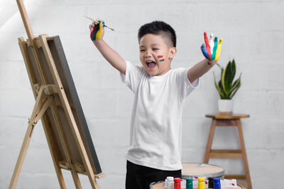 Messy boy celebrating by easel against wall