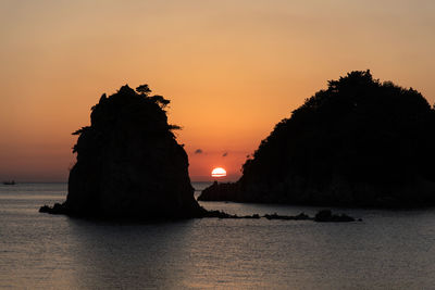 Silhouette rock in sea against sky during sunset