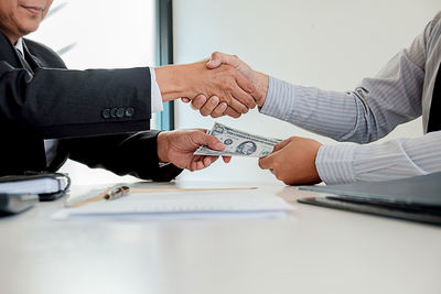 Midsection of businessmen shaking hands while taking bribe