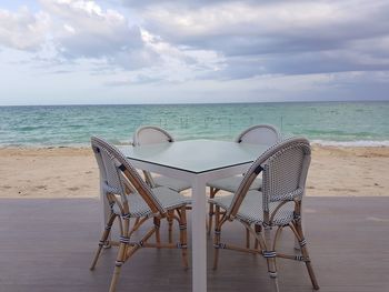 Deck chairs on beach against sky