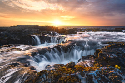 Scenic view of waterfall against sky during sunset