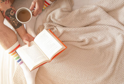 Man drinking coffee and reading a book in bed in the morning. rest concept.