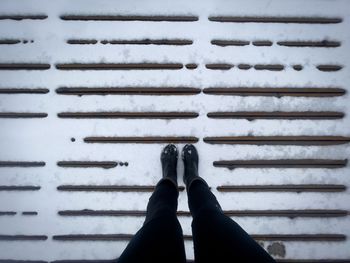 Personal perspective of female black boots standing on a wooden pontoon covered in snow