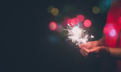 Midsection of woman holding illuminated christmas lights at night