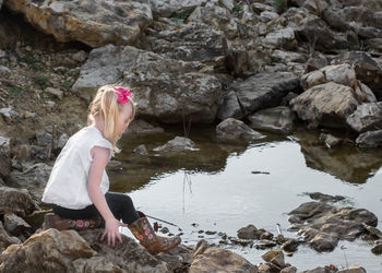 Side view of girl sitting on rock at lakeshore