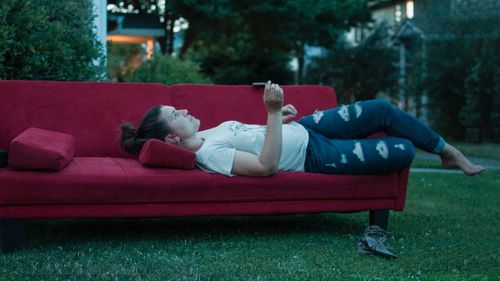 Side view of woman relaxing on sofa over field