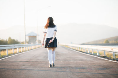 Rear view of young woman walking on road against sky