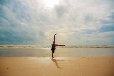 Man with arms raised on beach against sky