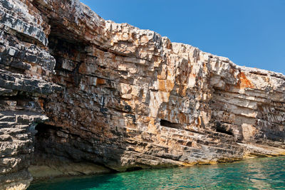 Layered structure of island vis. colored geological layers and turquoise water of adriatic sea.