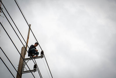 Low angle view of man sitting on ladder against sky