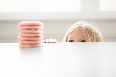 Blond girl peeking at stack of pink frosted sugar cookies on table