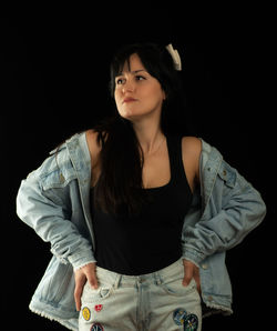 Young woman looking away while standing against black background