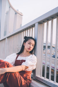 Portrait of young woman standing against railing