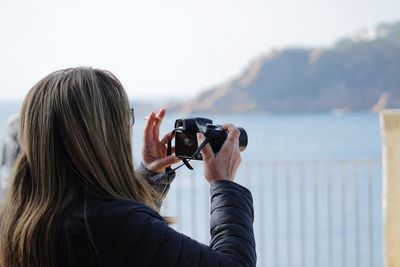 Rear view of woman photographing sea with digital camera