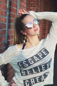 Young woman wearing sunglasses against brick wall