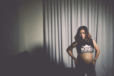 Portrait of pregnant woman standing against curtains at home