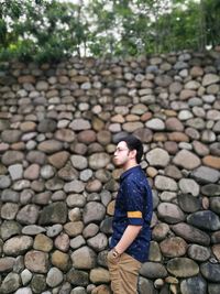 Side view of thoughtful man standing by stone wall