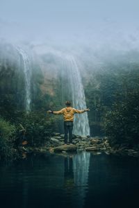 Man standing against waterfall in forest