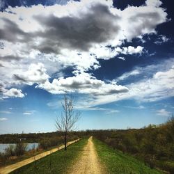 Road passing through field against cloudy sky