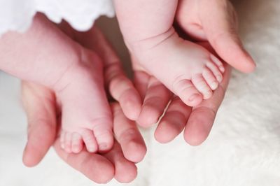 Cropped hands of parent holding baby barefoot