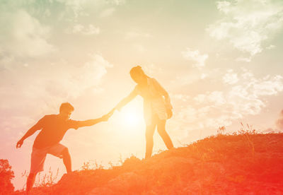 Man and woman with arms raised against sky during sunset