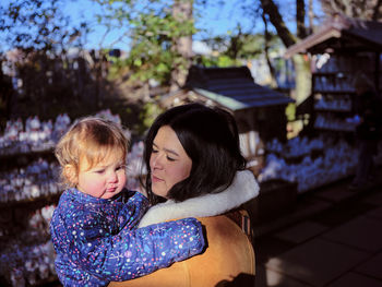 A young woman holds her infant child in the sun in an outdoor park.