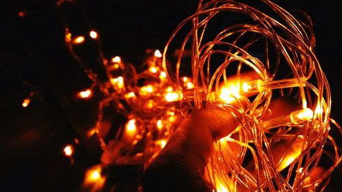 Cropped hand holding illuminated string light at night